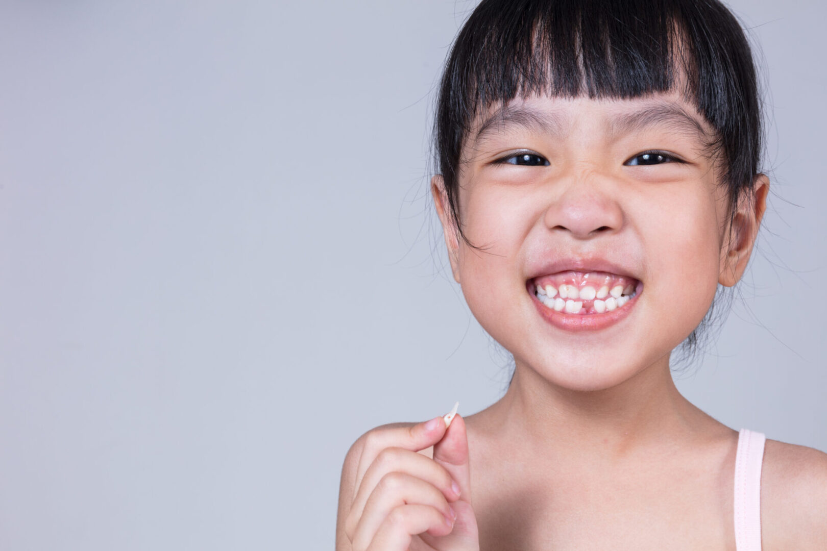 Asian Chinese little girl holding her missing tooth in isolated white background