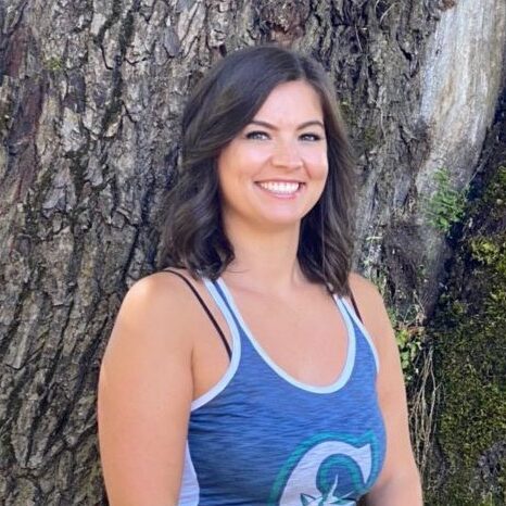 A woman standing in front of a tree smiling for the camera.